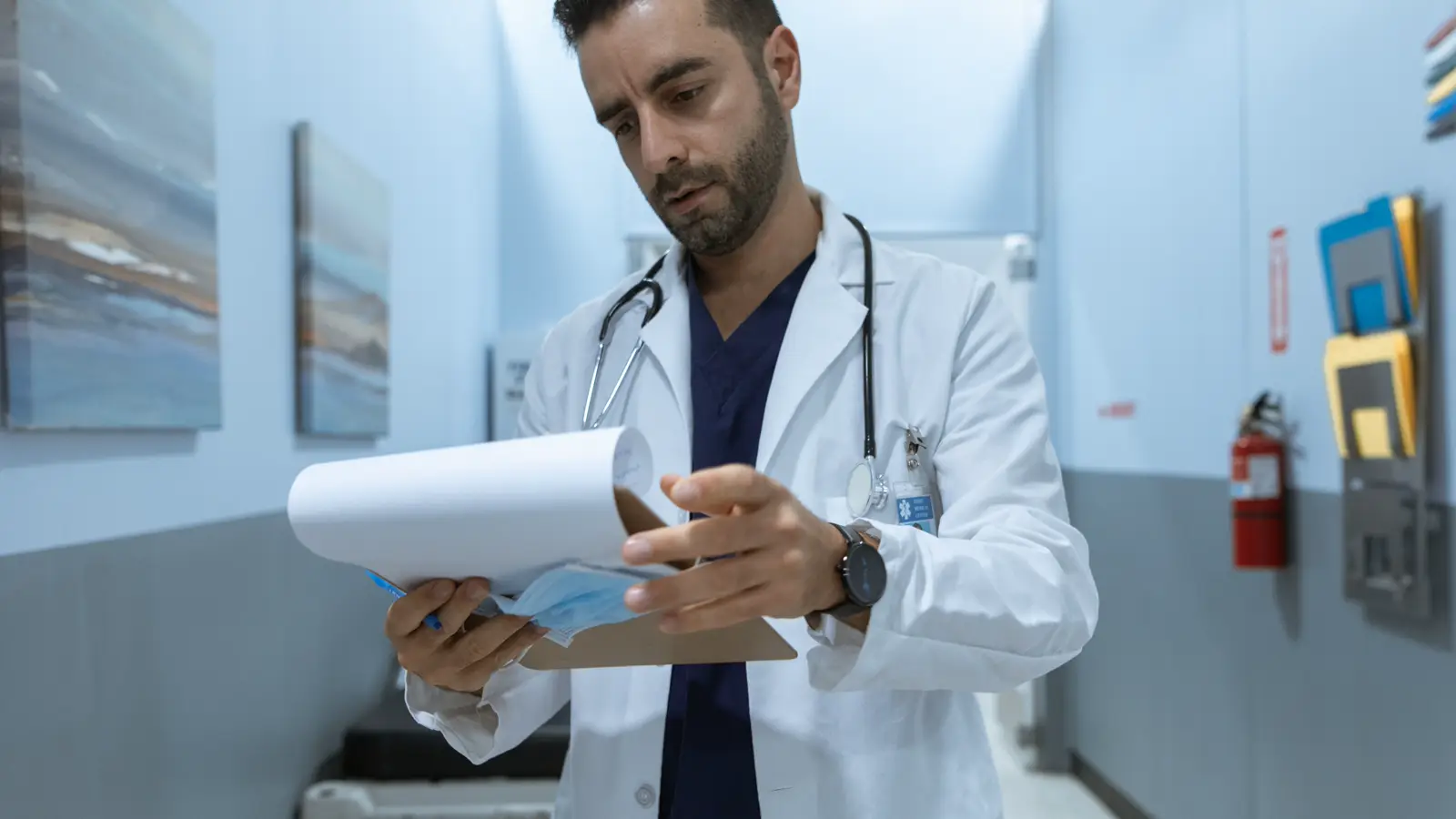 Médico de jaleco e estetoscópio analisa documentos em corredor de hospital, representando a revisão de um comunicado de cessação do auxílio-doença do INSS