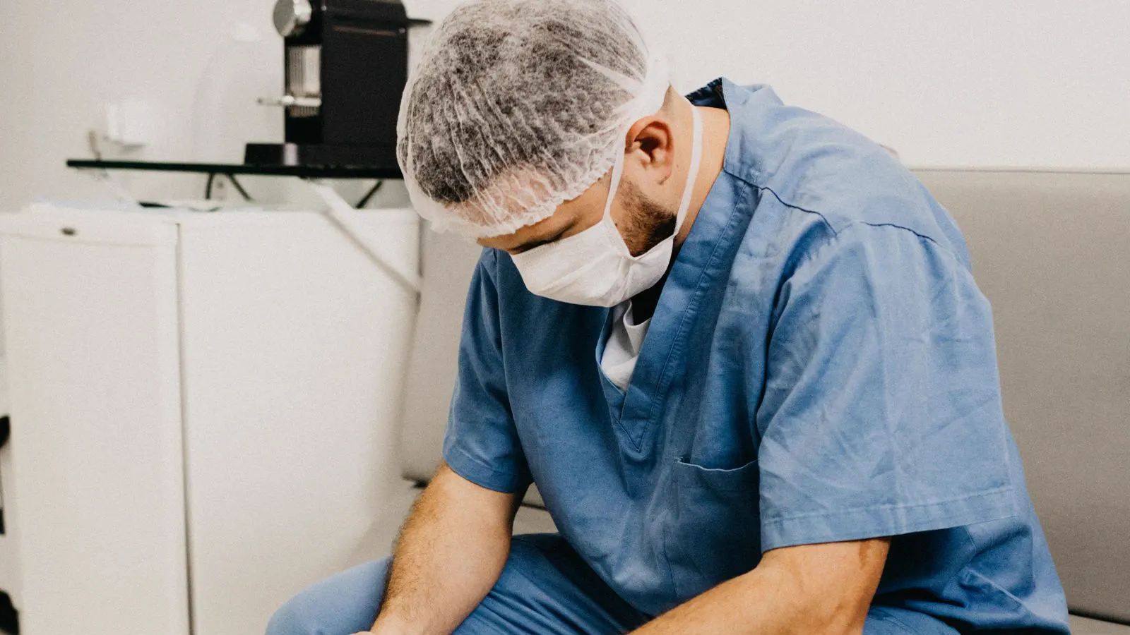 Médico de uniforme cirúrgico sentado com a cabeça baixa, exausto: burnout médico