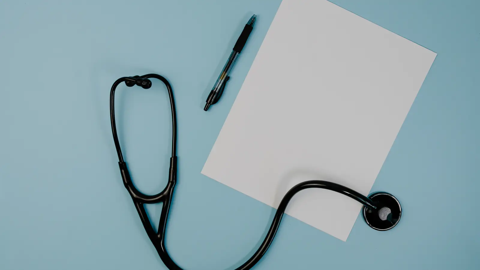 Estetoscópio, caneta e folha de papel em branco sobre superfície azul, representando a cobrança de honorários médicos atrasados pelo convênio