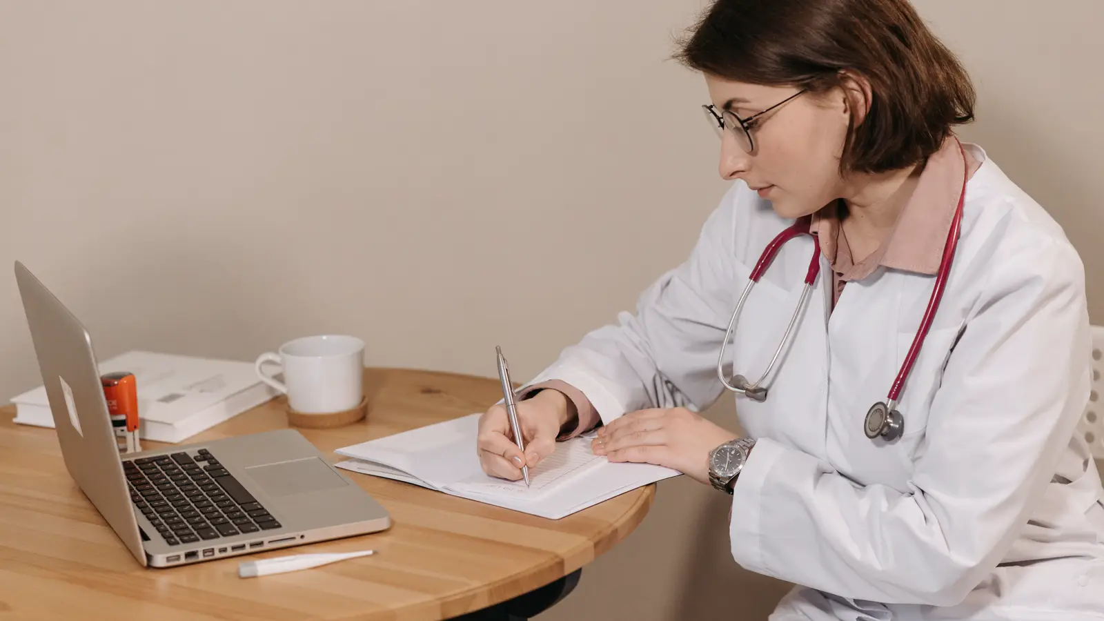 Médica estudando com livros e notebook sobre a mesa, representando a pós-graduação e os gastos com especialização médica