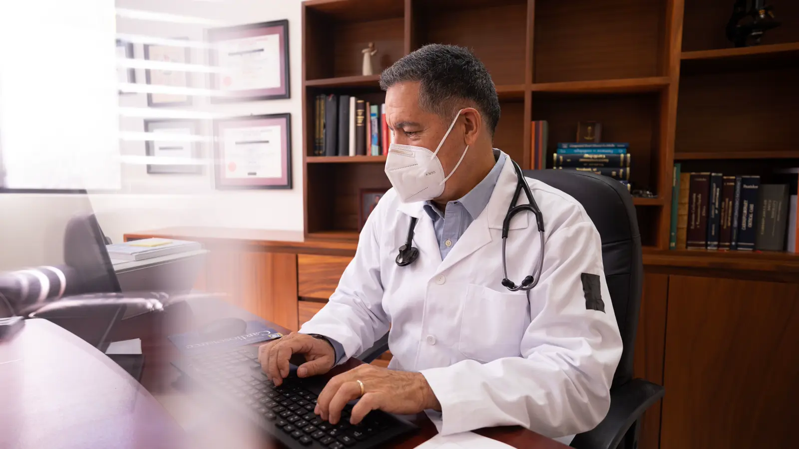 Médico de jaleco em consultório trabalhando no computador, representando direitos trabalhistas do médico CLT