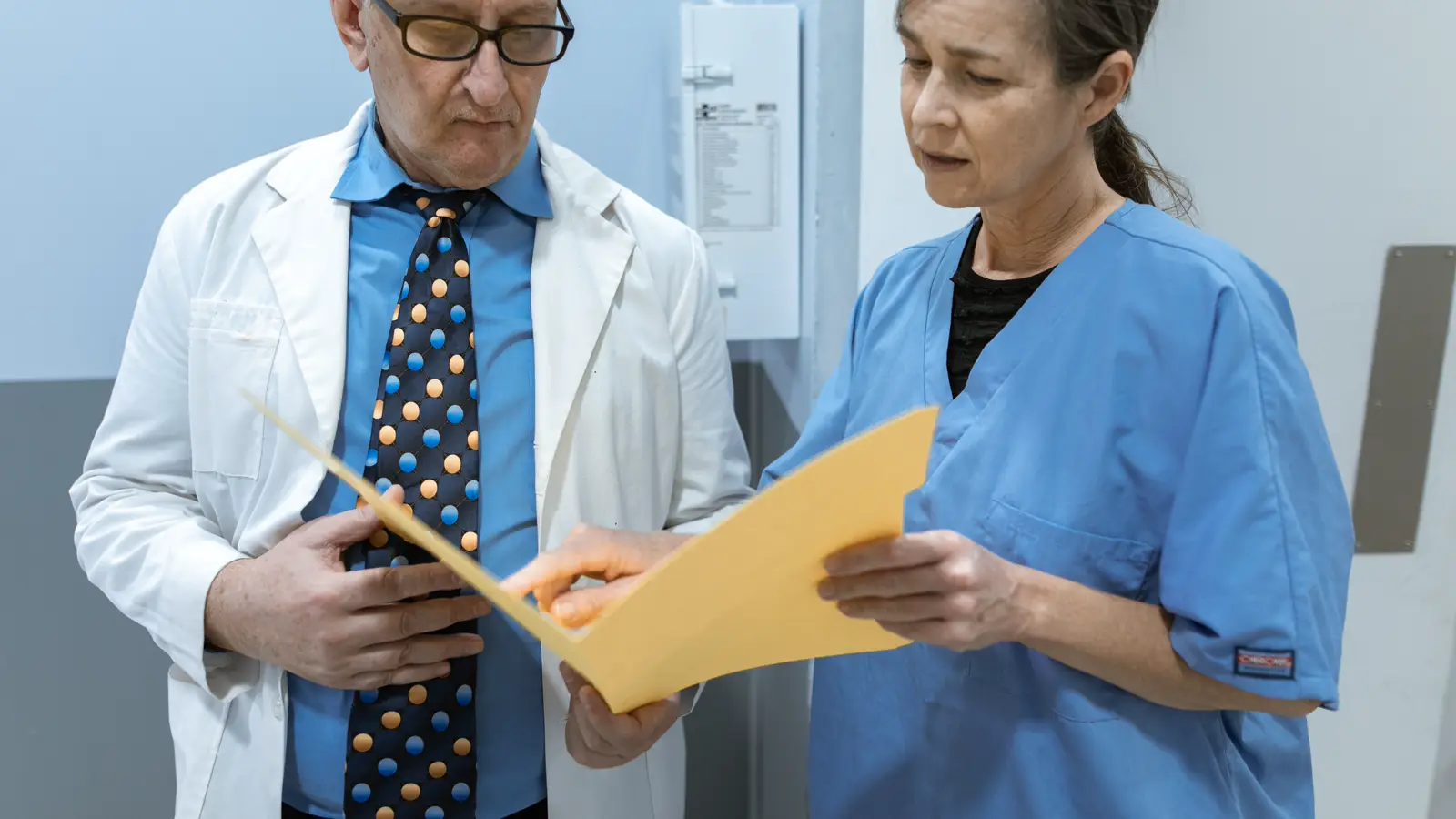 Médico de jaleco branco revisa pasta de documentos ao lado de colega em ambiente clínico