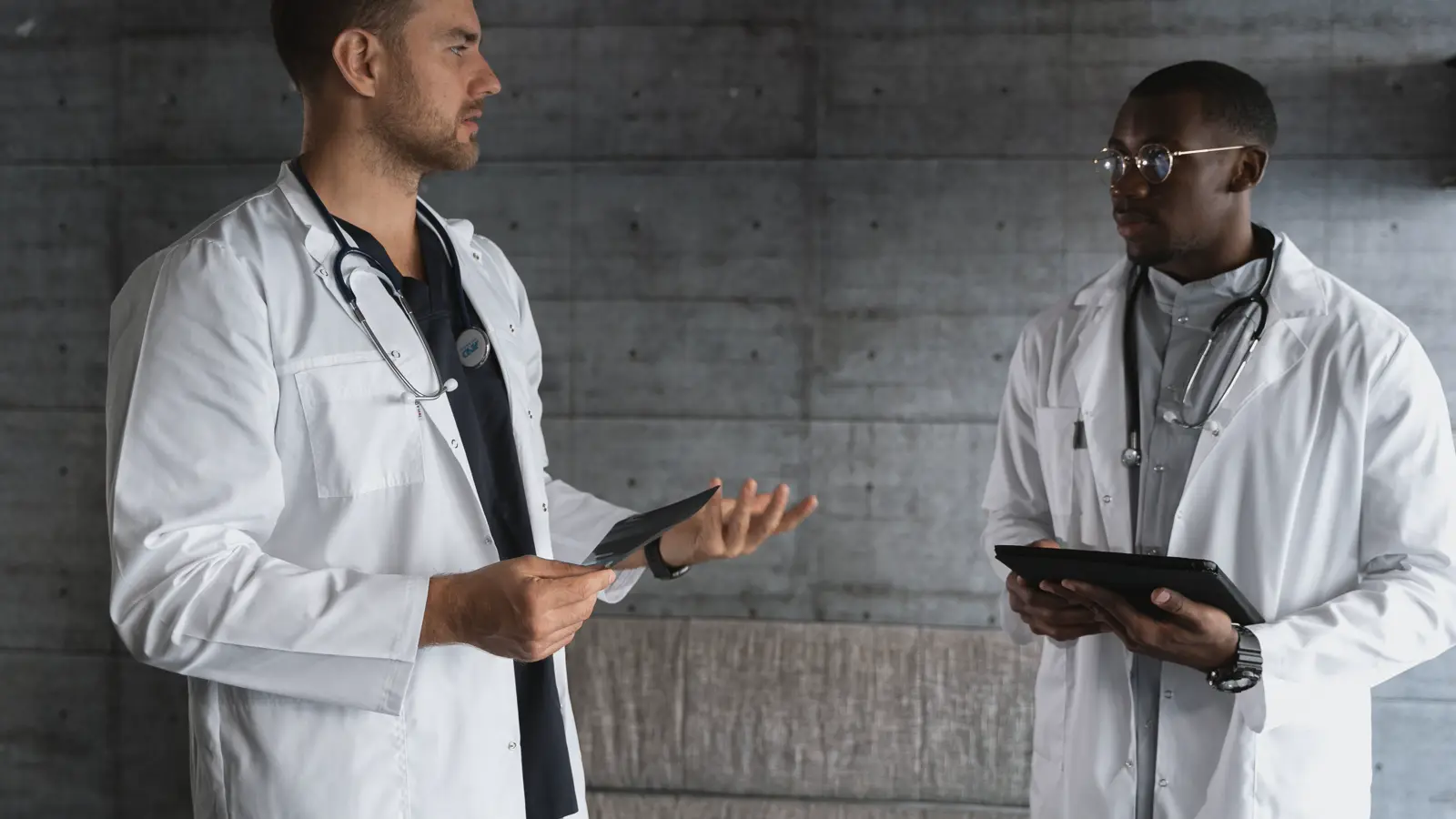 Dois médicos de jaleco branco comparando laudos e conversando sobre a diferença salarial entre a mesma função