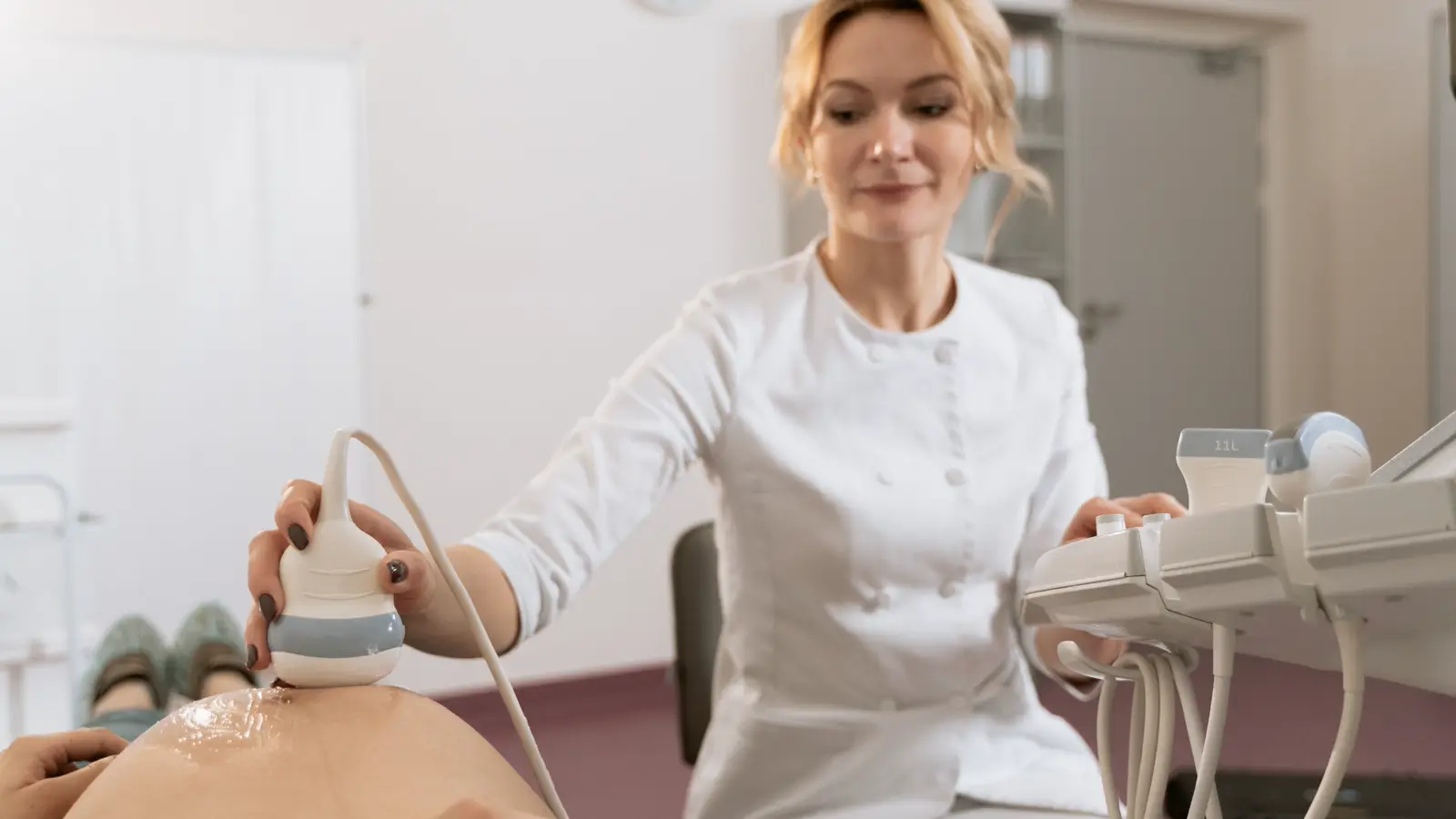 Médica de jaleco branco realizando ultrassom em paciente grávida, ilustrando os direitos da médica residente gestante