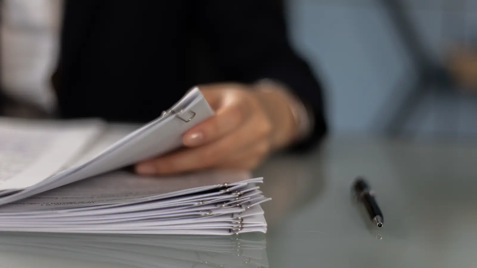 Mão organiza pilha de documentos grampeados sobre a mesa, com caneta ao lado, representando o termo de rescisão de contrato