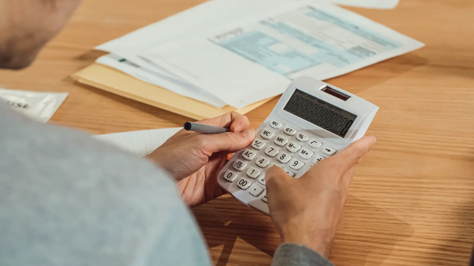 Mãos de médico cooperado usando calculadora sobre documentos financeiros para conferir o desconto de INSS e Imposto de Renda do repasse da cooperativa