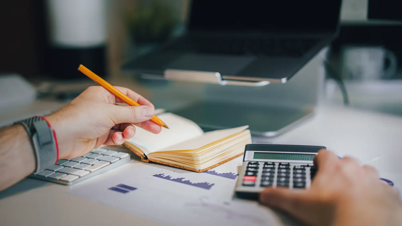Mãos calculando valores financeiros com calculadora e agenda sobre a mesa, representando o planejamento da contribuição do médico PJ ao INSS para garantir a pensão por morte da família