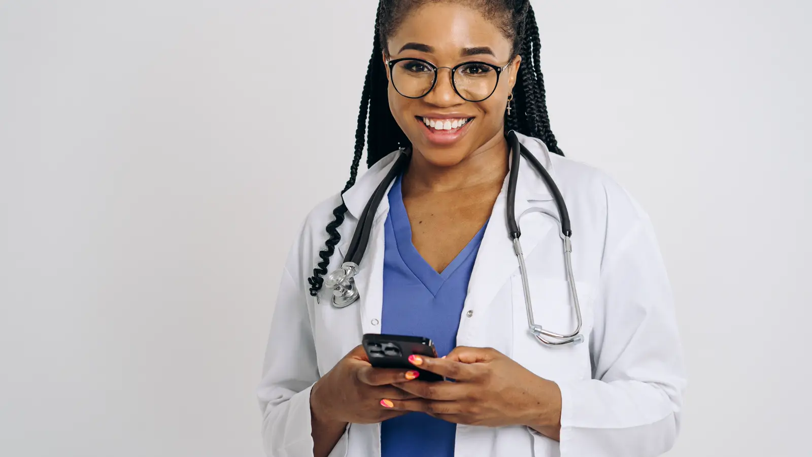 Médica de jaleco e estetoscópio sorri segurando o celular, ilustrando o uso do WhatsApp no contato com pacientes