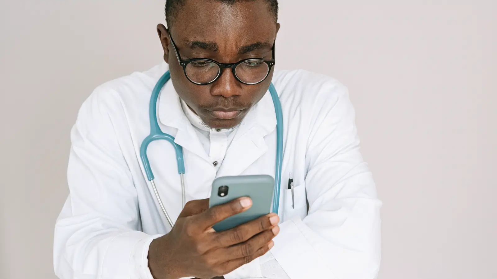 Médico de jaleco e estetoscópio olhando preocupado para avaliação no celular