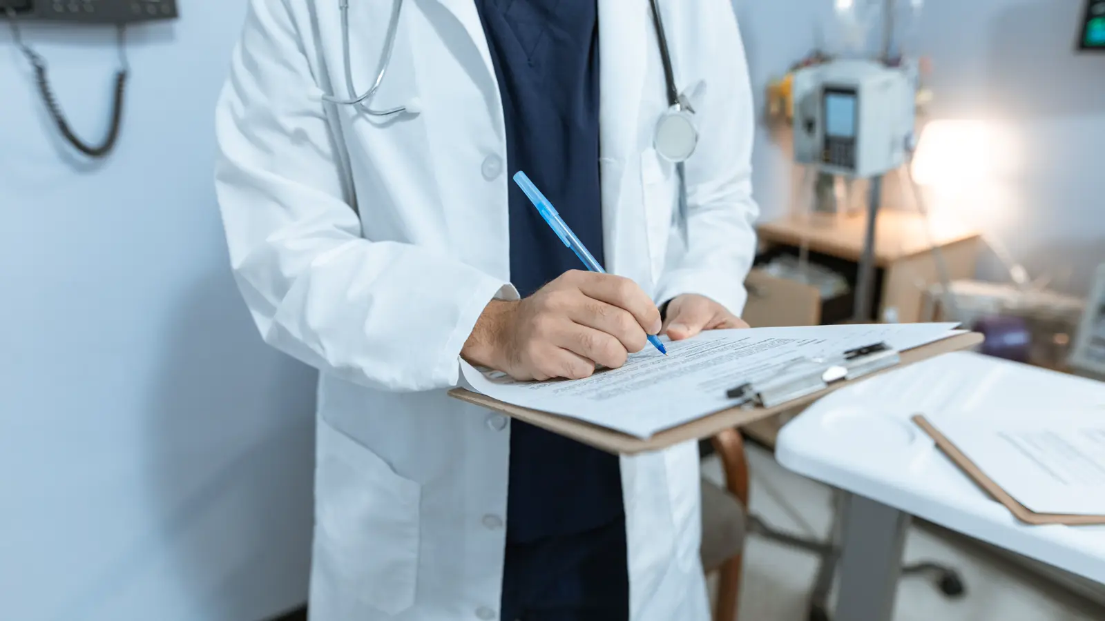 Médico de jaleco branco assinando documento em prancheta dentro de um consultório