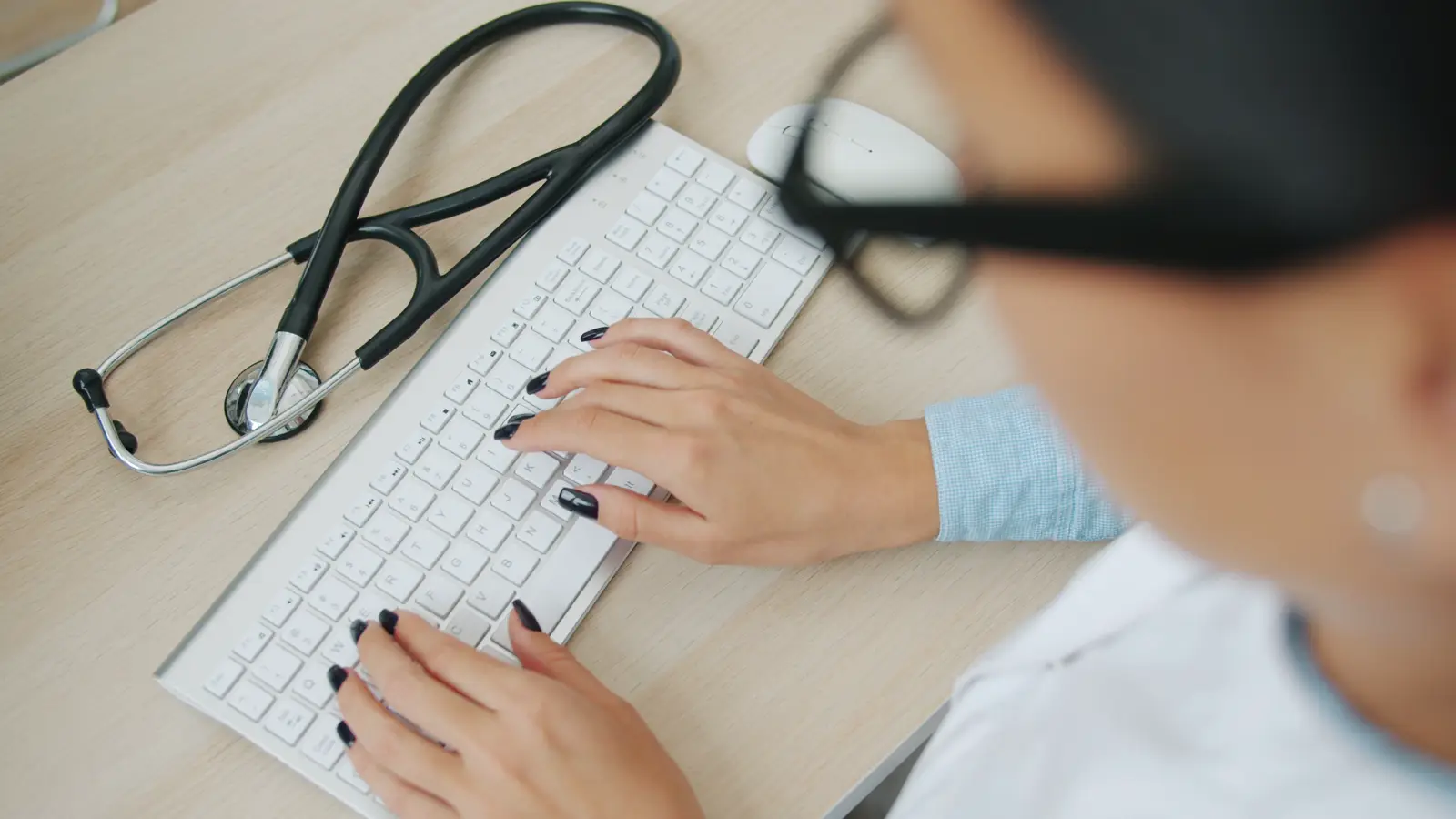 Médica com estetoscópio ao lado digitando em teclado de computador, ilustrando o uso de ChatGPT e outras ferramentas de IA no consultório