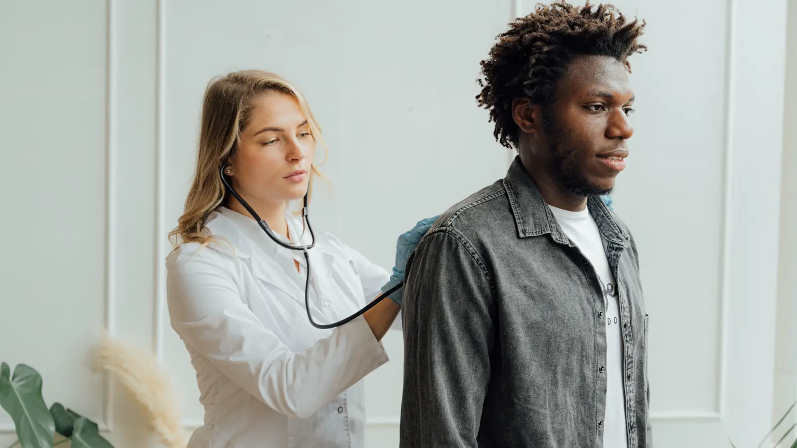 Médica com estetoscópio examinando as costas de um paciente em consultório, ilustrando o exame ocupacional do PCMSO na medicina do trabalho