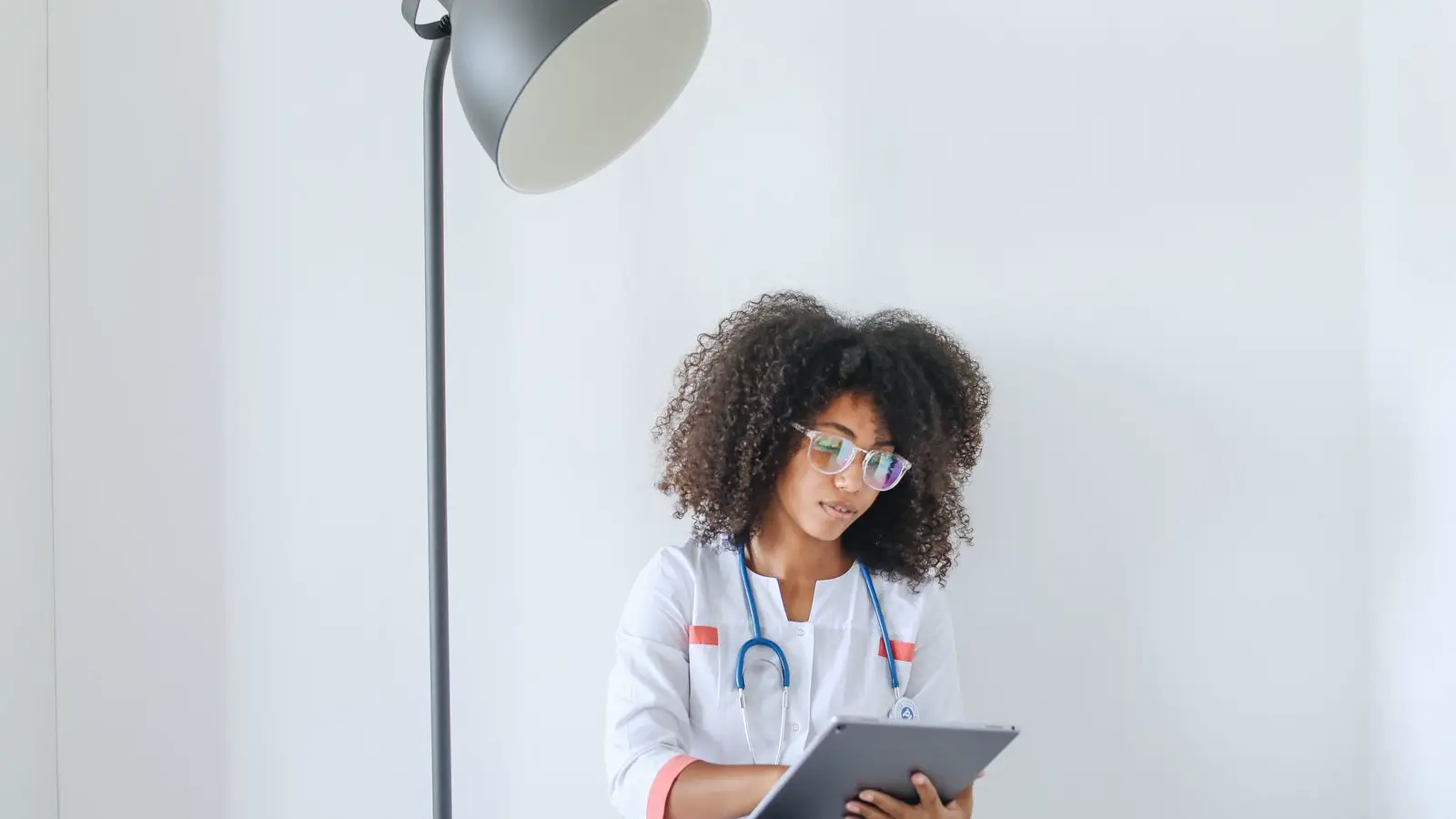Médica de jaleco e estetoscópio consultando dados de prontuário eletrônico em tablet, ilustrando o compartilhamento de dados com apps de gestão de clínica sob a LGPD