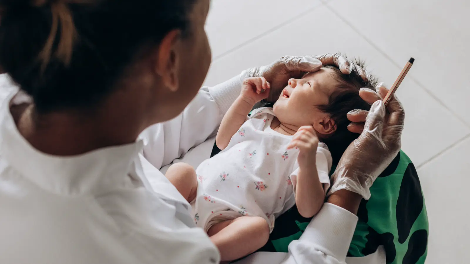 Médica residente de jaleco branco segura bebê recém-nascido no colo em corredor de hospital, ilustrando a prorrogação da residência médica após a licença-maternidade