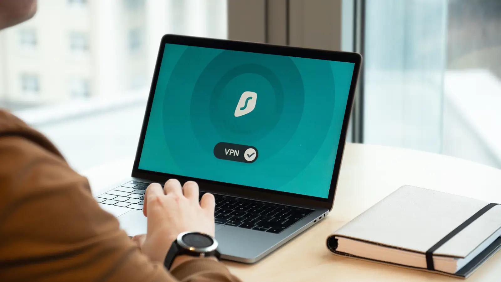 Pessoa digitando em notebook com tela mostrando ícone de VPN e segurança de rede, ilustrando proteção contra ataque de ransomware e vazamento de dados de pacientes na clínica médica